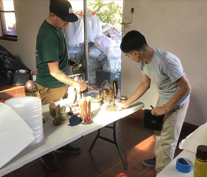 Two male SERVPRO employees standing around a table filled with objects from client's home