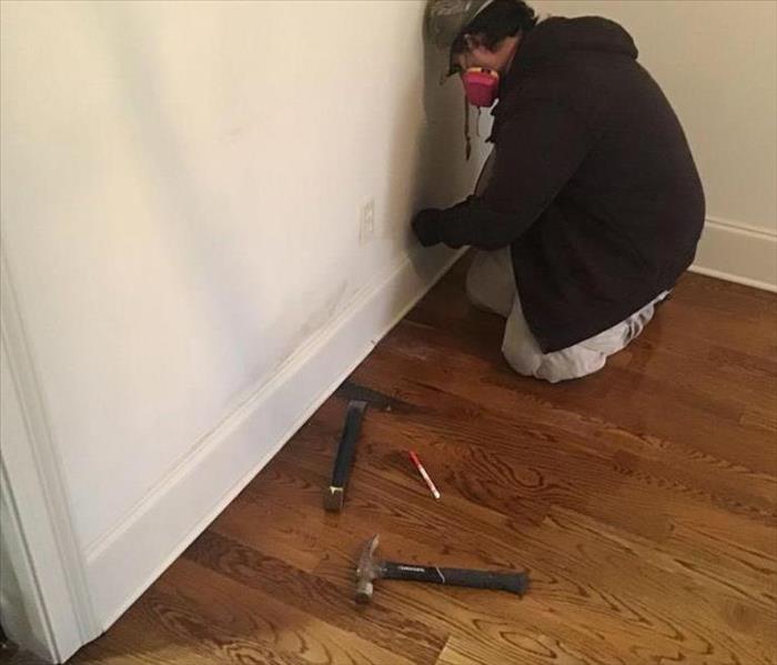 male employee looking at white wall with two hammers on the floor