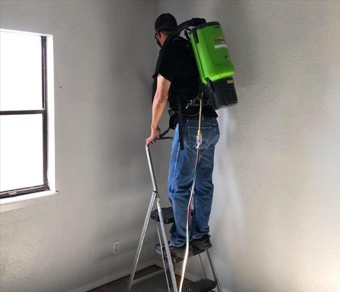 male SERVPRO employee using HEPA vacuum to clean ceiling and walls
