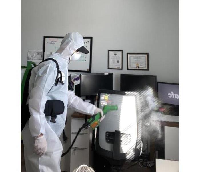 male SERVPRO employee cleaning and disinfecting using a sprayer in full PPE.